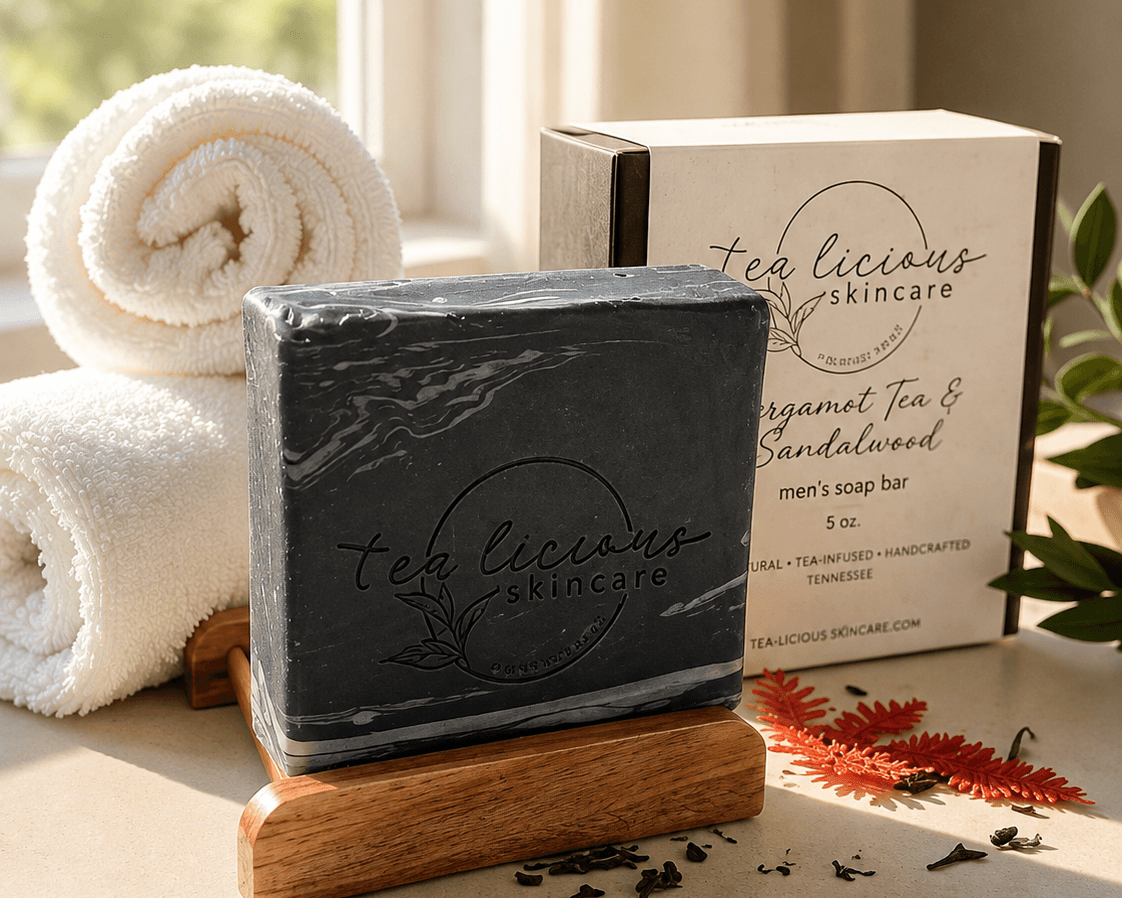 Tea-licious Black Tea & Sandalwood tea-infused men’s soap with a black marbled design displayed on a wooden soap dish beside its product box in warm natural light.
