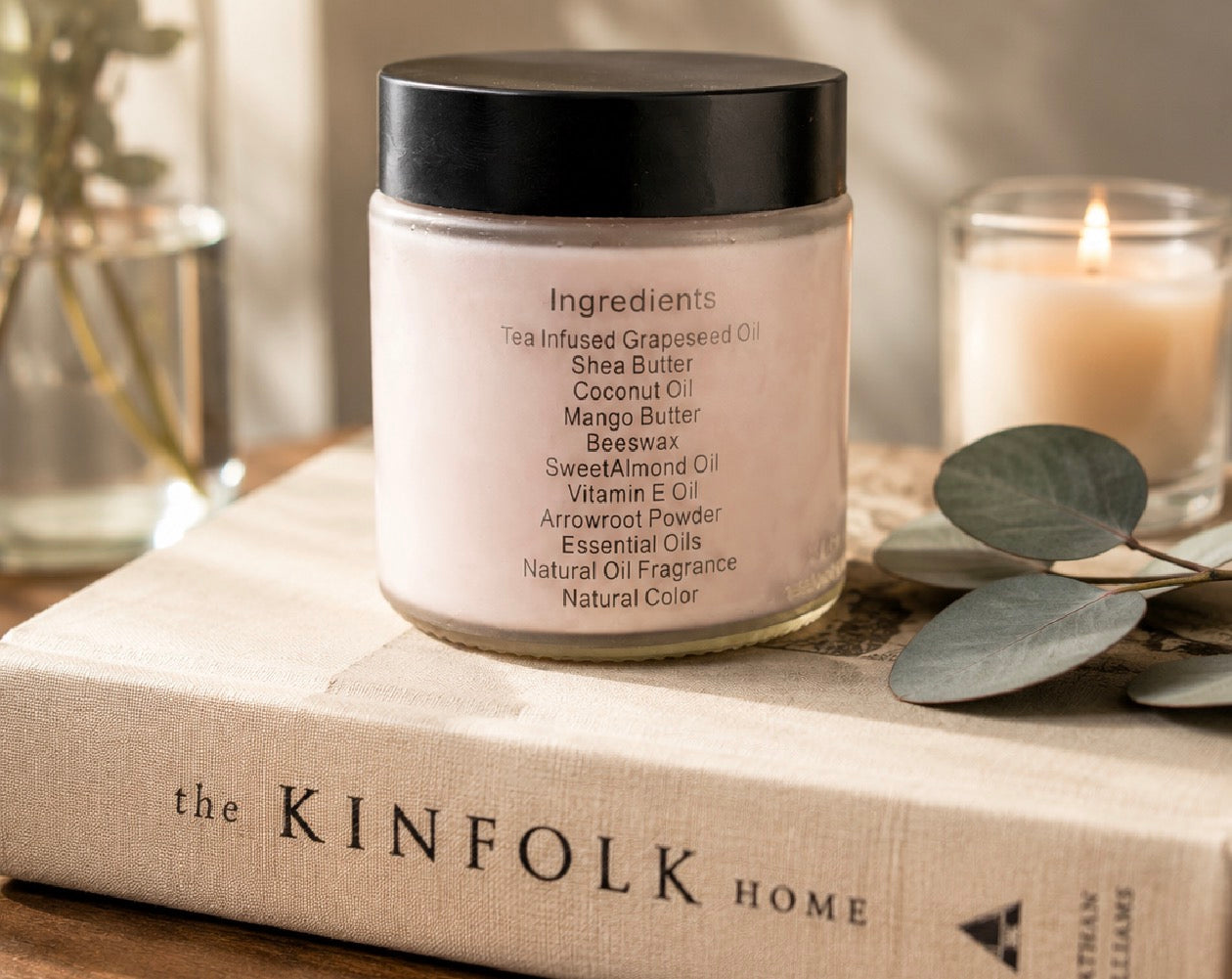 Tea-licious skincare Jar of body cream with ingredients showing on a book with a candle in the background