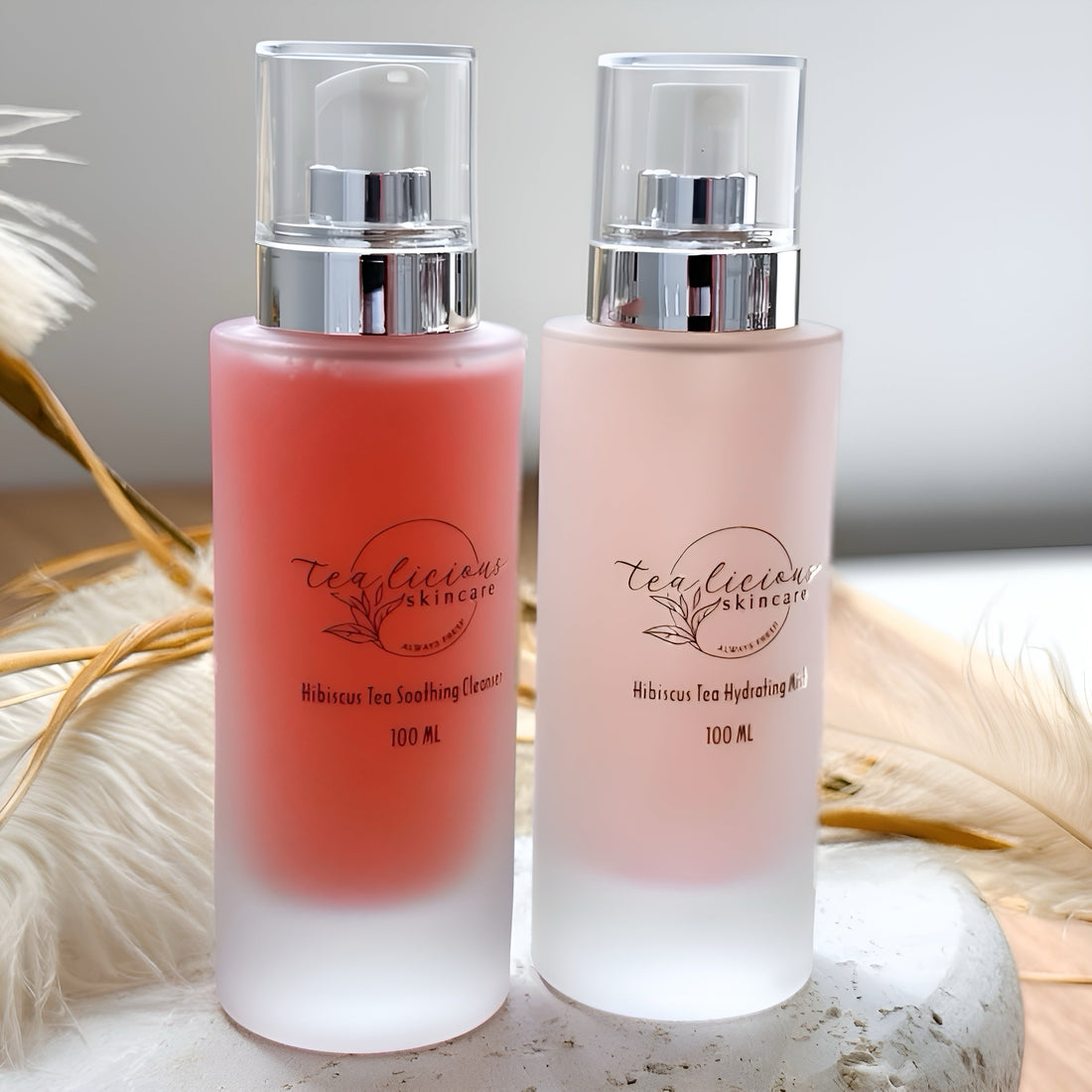 Frosted glass bottles of pink Hibiscus Tea Soothing Serum and pale pink Hydrating Mist by Tea-liciouskincare—pure, non-toxic tea blends for soothing and hydrating sensitive skin.