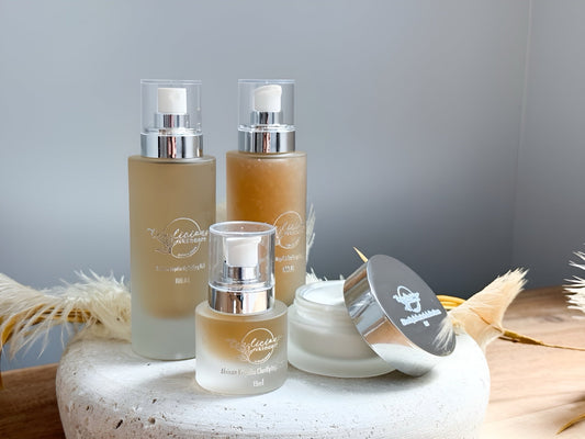 Tea-Licious African Kigelia Clarifying skincare set: beige-toned pump bottles and silver-lidded balm jar on wooden surface, designed for natural acne care and balanced skin.