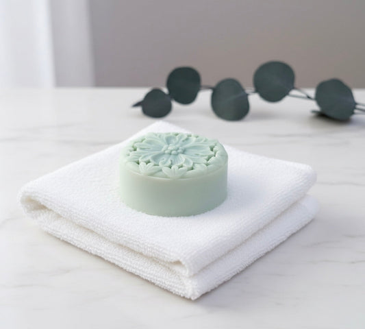 Waterless skincare solid lotion bar on folded towel with soft eucalyptus leaves minimal background