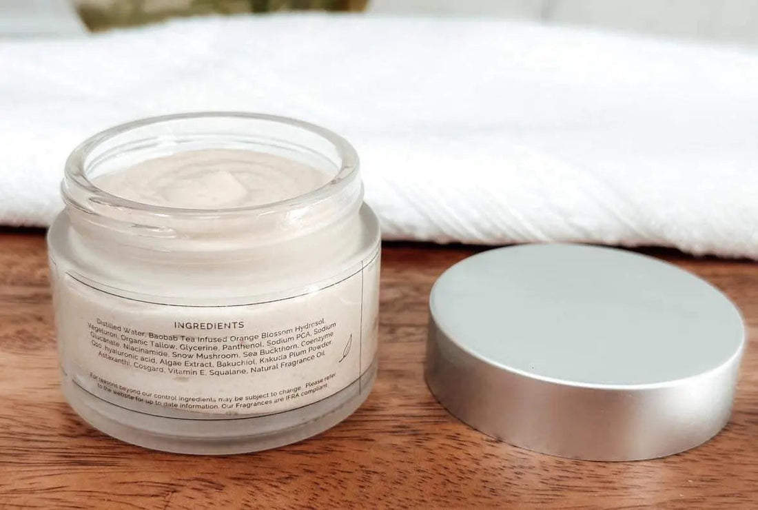Open jar of tea-infused moisturizer with lid beside it on wooden surface in natural light glow tones