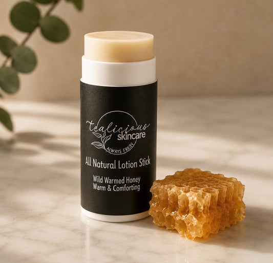 Tea-licious Skincare Wild Warmed Honey lotion stick displayed on a marble surface beside a piece of golden honeycomb