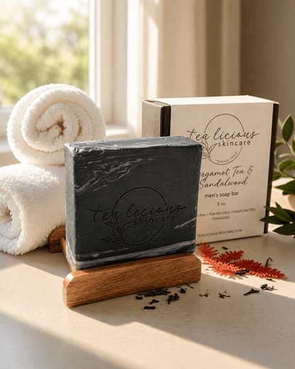Tea-licious Black Tea & Sandalwood tea-infused men’s soap with a black marbled design displayed on a wooden soap dish beside its product box in warm natural light.