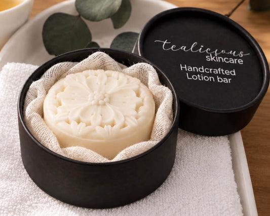 Creamy vanilla Solid Lotion Bar nestled in soft gauze inside a black Tea-Licious Skincare container, styled with warm natural light, tea, and neutral spa-inspired accents.
