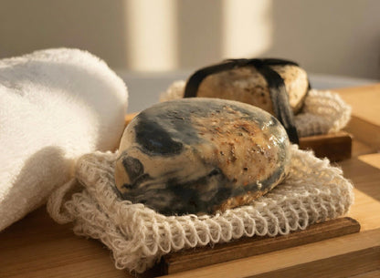 Charcoal tea soap resting on natural cloth with warm sunlight and botanical spa-inspired styling.