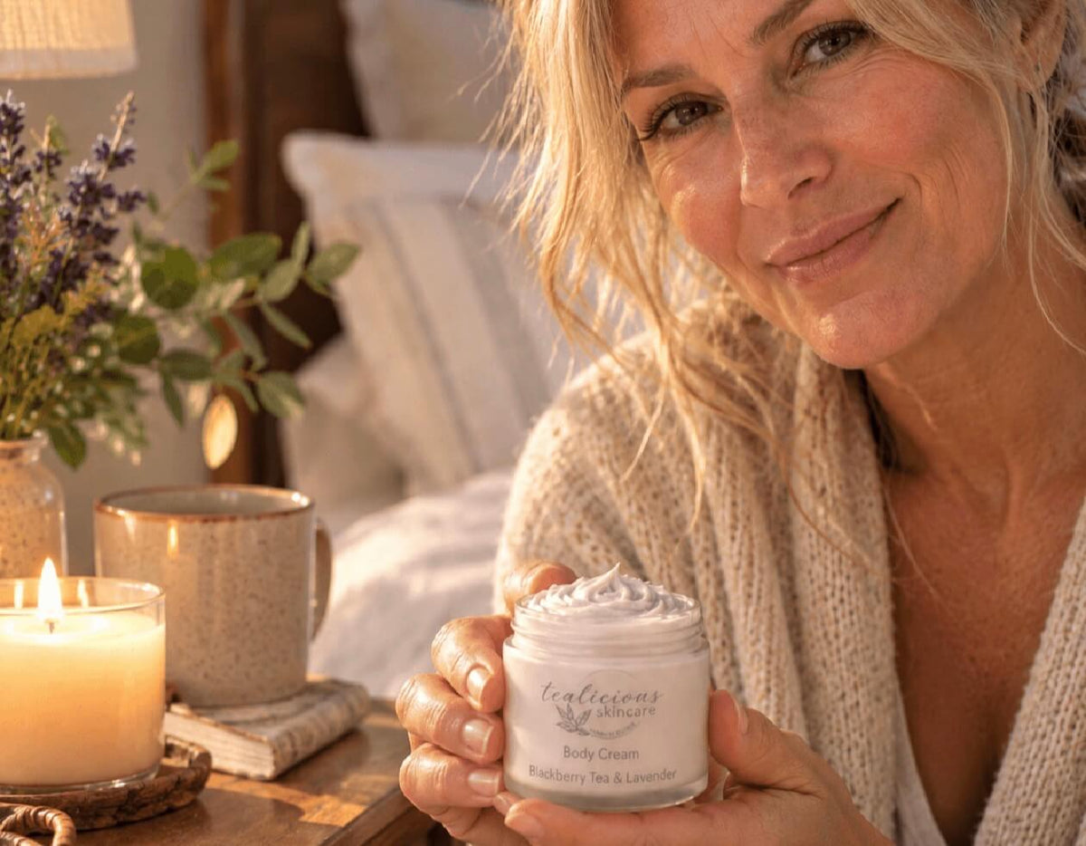 Mature woman holding Tea-Licious tea-licious Skincare Blackberry Tea & Lavender Body Cream beside a candle in a warm bedroom setting.
