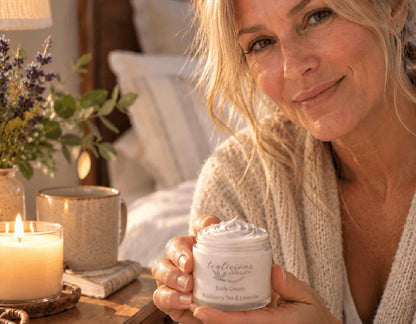 Mature woman holding Tea-Licious tea-licious Skincare Blackberry Tea & Lavender Body Cream beside a candle in a warm bedroom setting.