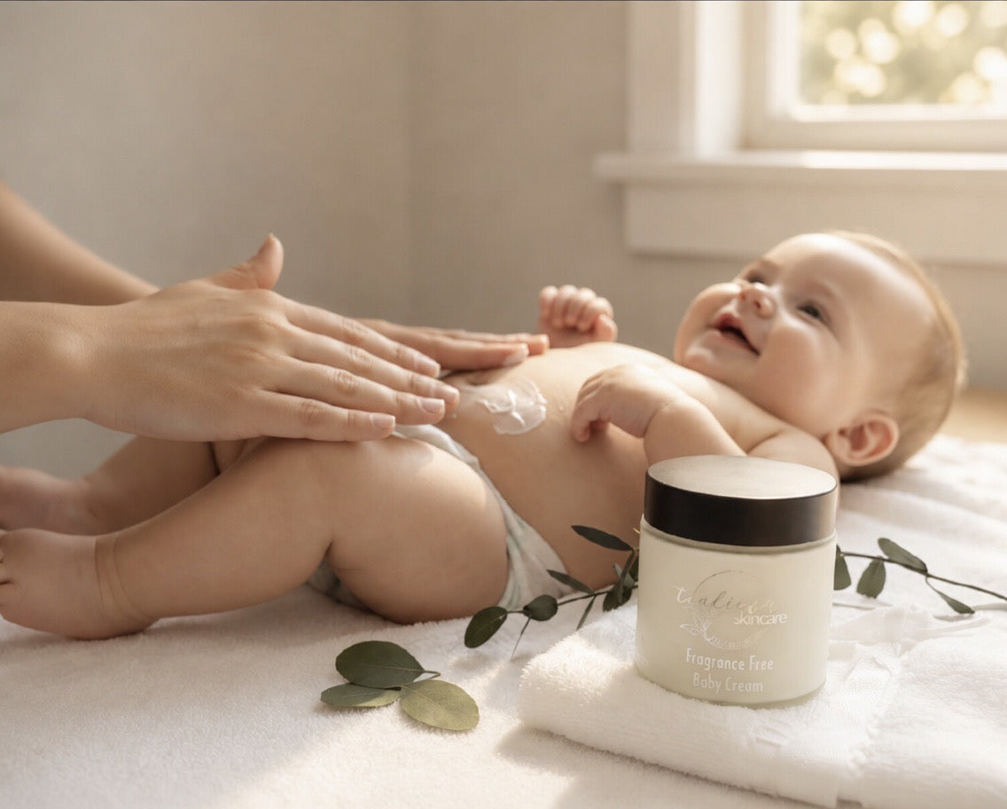 Baby lying on a towel with a jar of baby lotion next to it, in a softly lit room.