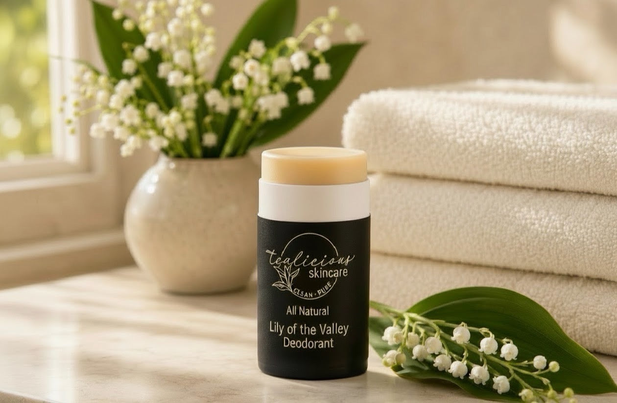 Tea-licious skincare Lily of the Valley All Natural Deodorant stick standing on a marble bathroom counter next to fresh lily of the valley flowers and stacked white towels, bathed in warm morning side-window sunlight