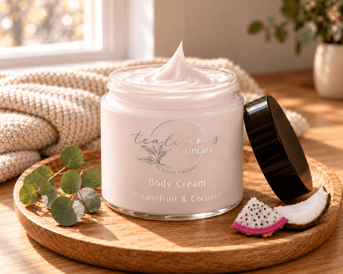Open jar of Tea-licious Dragonfruit & Coconut Body Cream on a wooden tray with dragonfruit, coconut and a cream knit blanket.