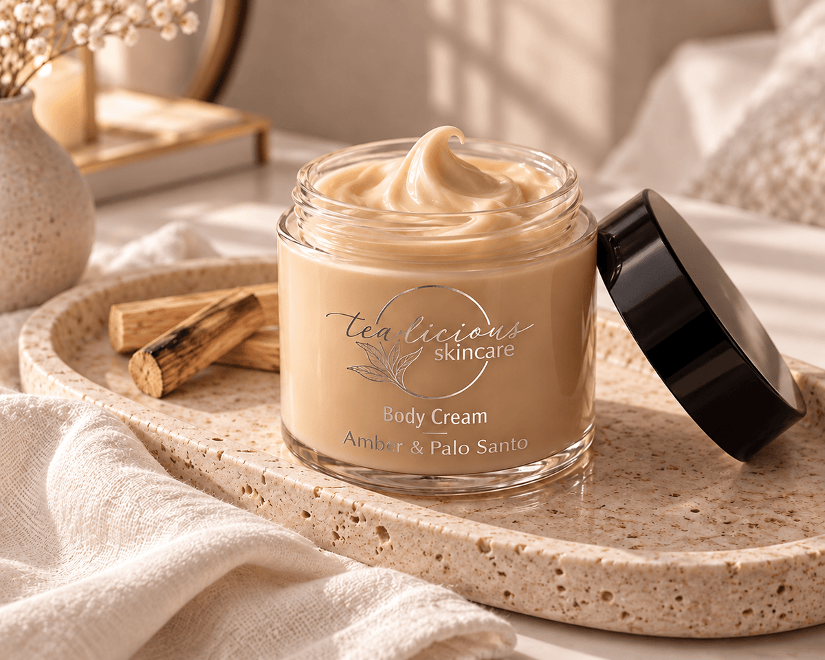 Open jar of Tea-licious Amber & Palo Santo Body Cream showing its light toffee colour on a stone tray beside soft linen and Palo Santo wood.