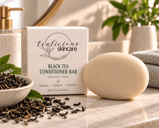 Black Tea Conditioner Bar for oily hair with Tea-Licious Skincare packaging and a subtle pink hibiscus accent on a wet shower ledge.