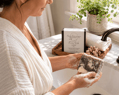 Woman lathering Tea-Licious Black Tea & Creamy Milk Soap at a bathroom sink with the packaged soap displayed behind her.