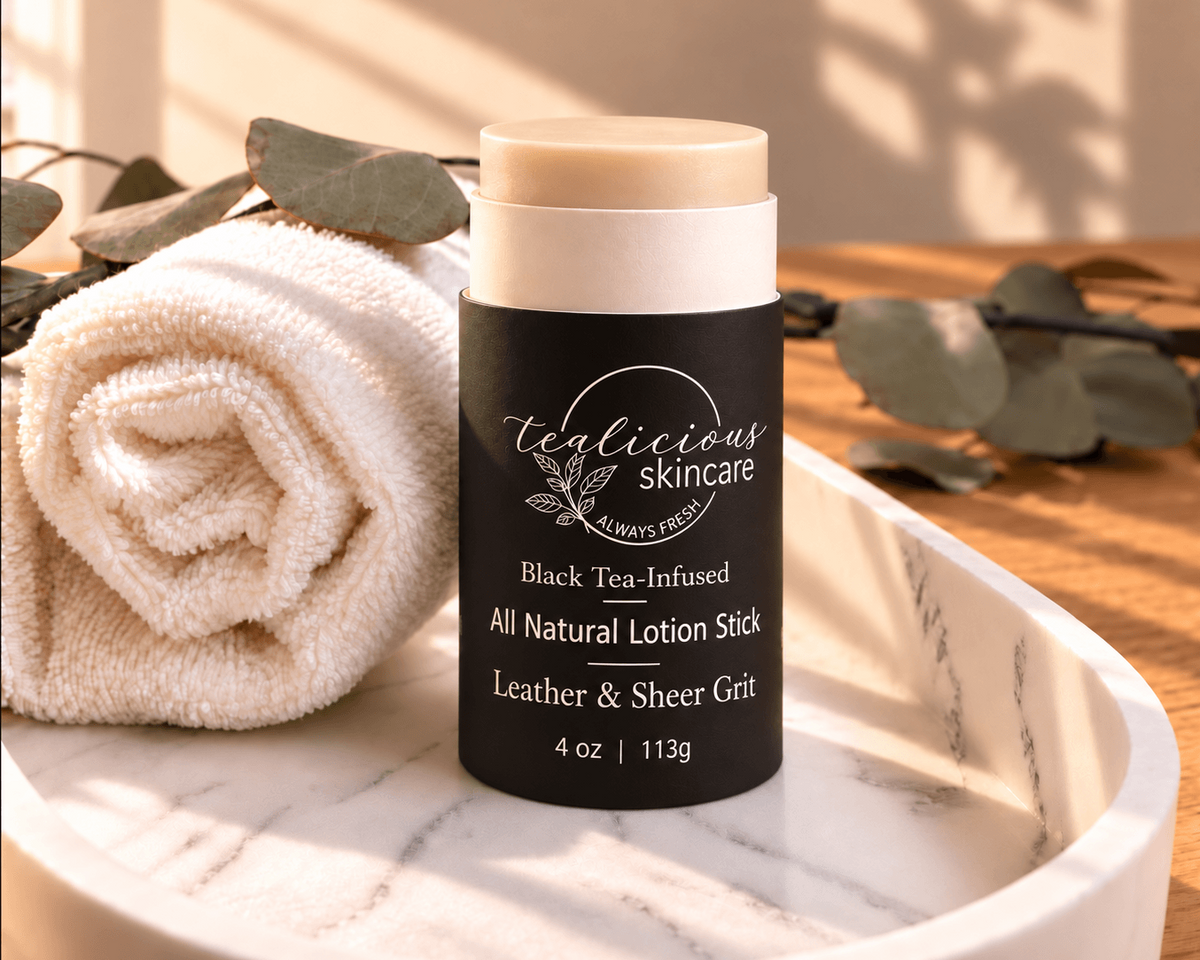 Tea-Licious Black Tea-Infused Leather & Sheer Grit men’s solid lotion stick on a marble tray in warm natural light with a rolled towel and eucalyptus.