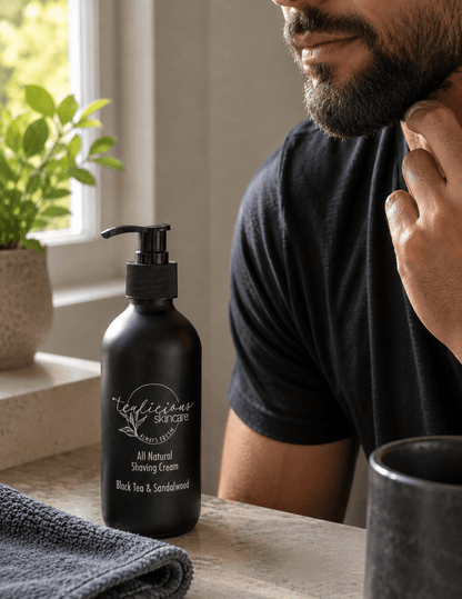 Man with a well-groomed beard touching his neck after shaving beside Tea-licious Black Tea & Sandalwood tea-infused shaving cream on a bathroom vanity in natural morning light.