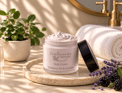 Tea-Licious Blackberry Tea & Lavender Body Cream on a stone tray with lavender, blackberries and soft towels in warm natural light.