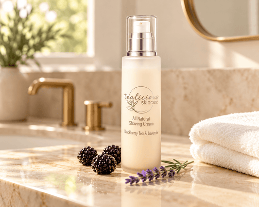Tea-licious Blackberry Tea & Lavender shaving cream bottle on a warm marble bathroom vanity beside folded white towels.