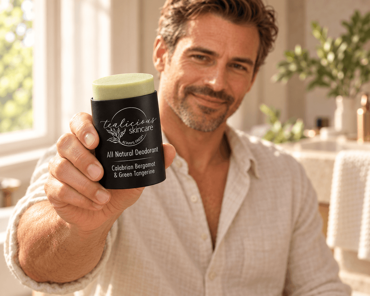 Smiling man holding Tea-licious Calabrian Bergamot & Green Tangerine deodorant toward the camera, showing its black oval container and silver label.