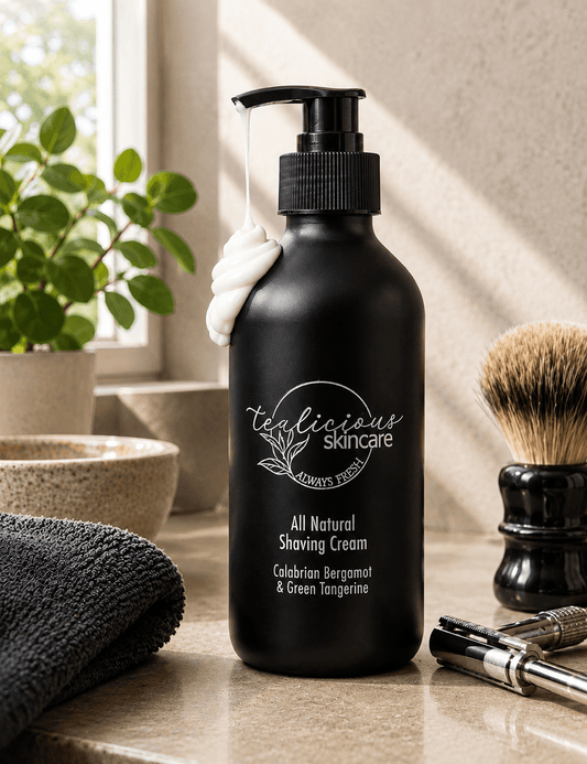 Tea-infused Calabrian Bergamot & Green Tangerine shaving cream in a black pump bottle with a rich cream swirl, displayed beside a shaving brush and safety razor on a sunlit bathroom countertop.