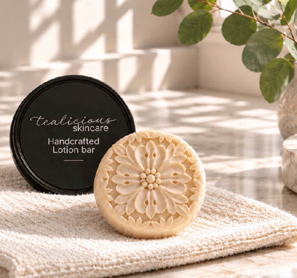 Cocoa Butter & Cashmere tea-infused lotion bar with handcrafted floral design beside its tin on a folded towel, providing concentrated waterless moisture for dry skin.