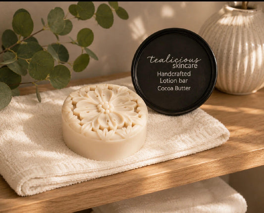 Cocoa Butter & Cashmere tea-infused lotion bar with handcrafted floral design beside its tin on a folded towel, providing concentrated waterless moisture for dry skin.