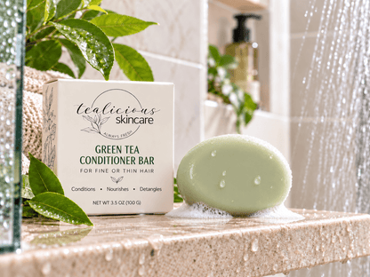 Green Tea Conditioner Bar for fine or thin hair shown beside its box on a wet bathroom ledge under running water.