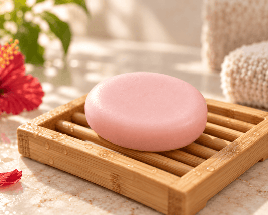 Smooth light pink Tea-Licious Hibiscus Tea Conditioner Bar resting on a bamboo drying rack in a warm bathroom setting.