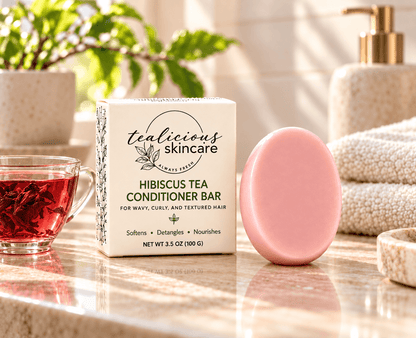 Tea-Licious Hibiscus Tea Conditioner Bar for wavy, curly and textured hair beside its cream box and pink hibiscus flower in warm natural morning light.