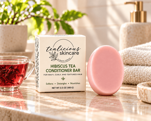 Tea-Licious Hibiscus Tea Conditioner Bar for wavy, curly and textured hair beside its cream box and pink hibiscus flower in warm natural morning light.