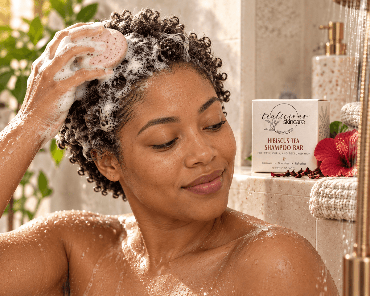Woman with short curly hair using Tea-Licious Hibiscus Tea Shampoo Bar in the shower, with rich lather and the shampoo box displayed beside her.