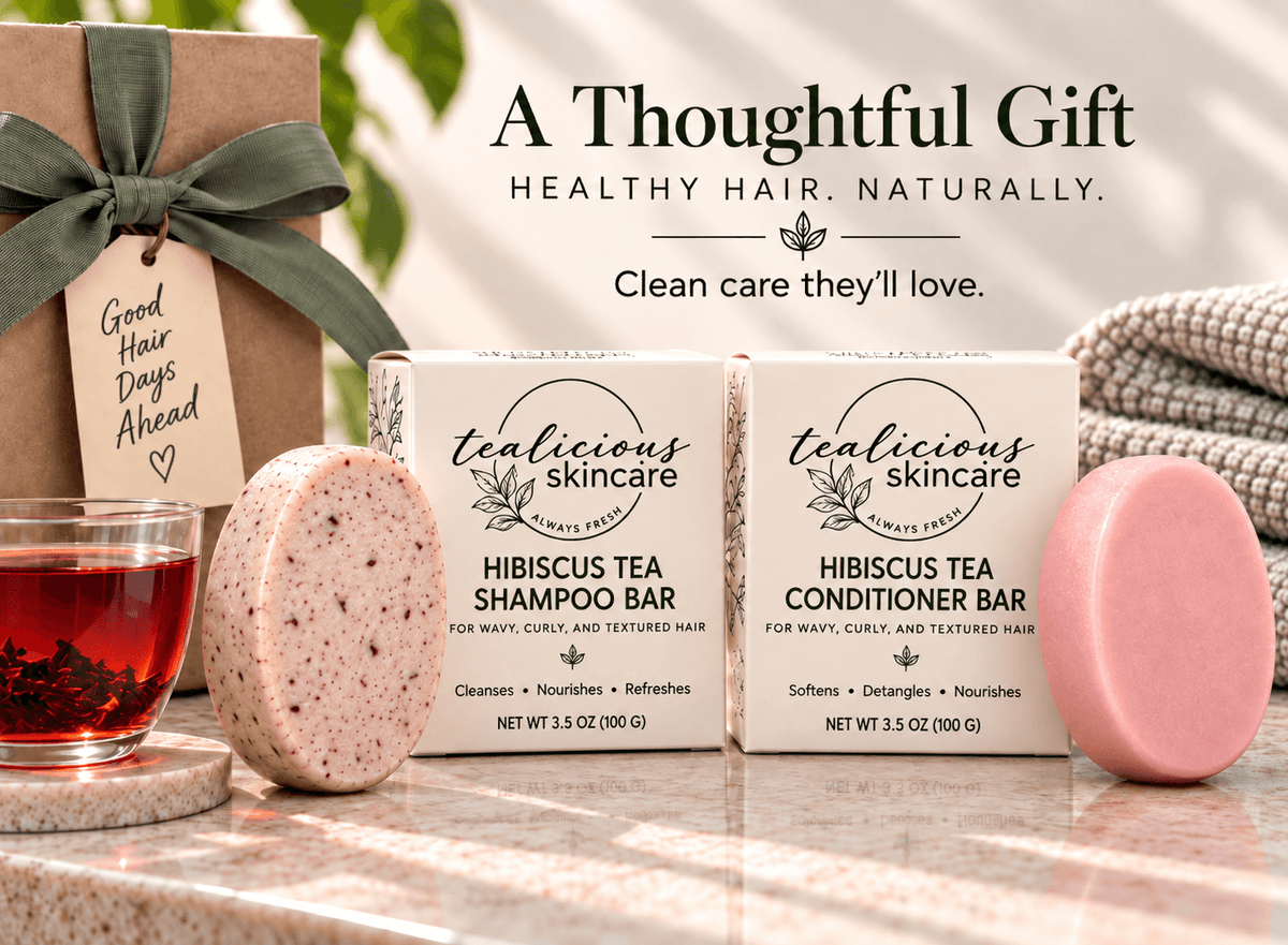 Tealicious Skincare Hibiscus Tea Shampoo Bar and Conditioner Bar gift set displayed with their packaging boxes, a wrapped gift box, a glass of red tea, and a pink shampoo bar on a marble surface.