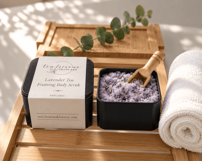 Tea-Licious Lavender Tea Foaming Body Scrub in black tins with lavender scrub, wooden scoop and rolled towel on a bamboo bath tray.