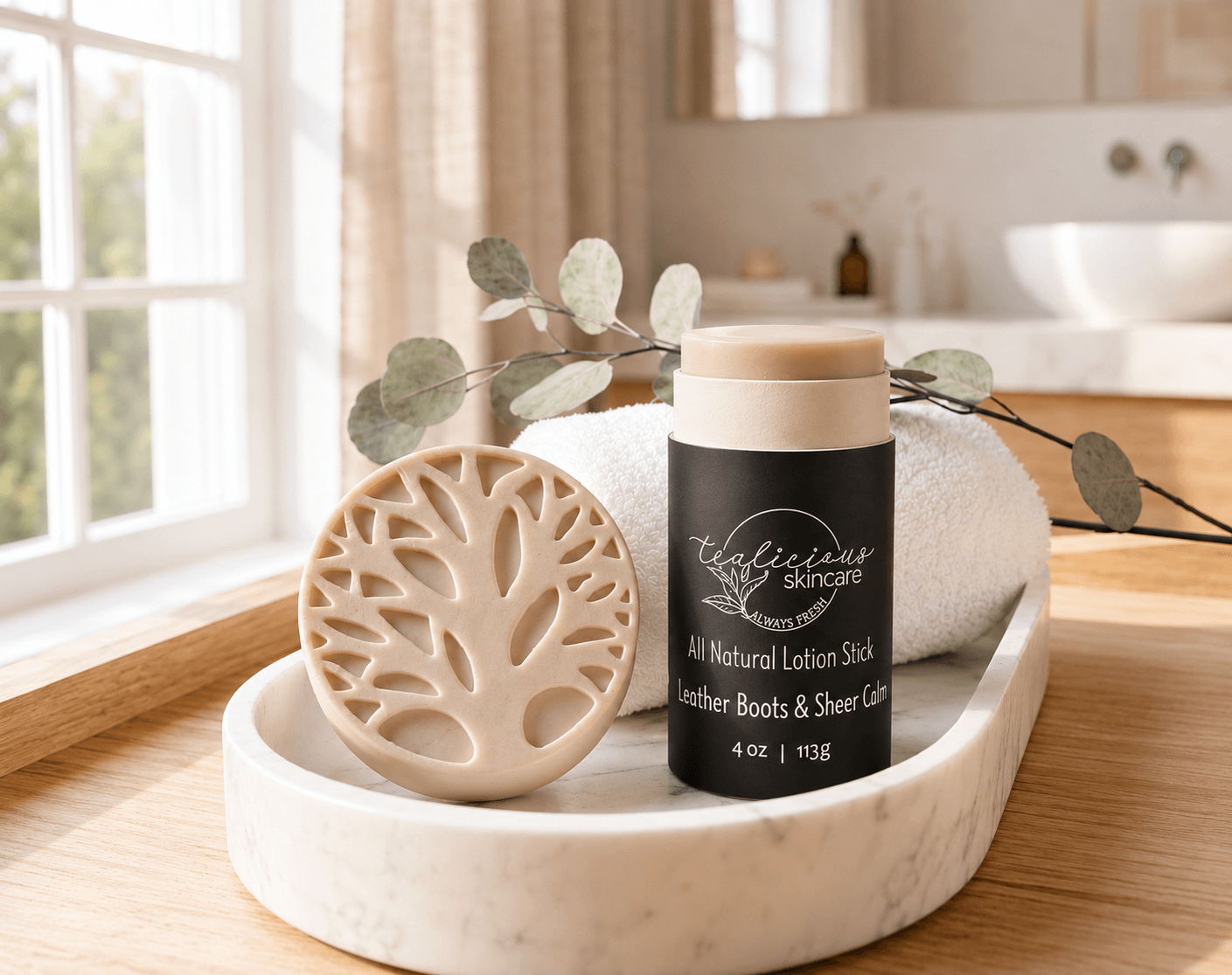 Tea-licious Skincare Leather Boots and Grit all-natural lotion stick on a marble vanity next to a rolled white towel.