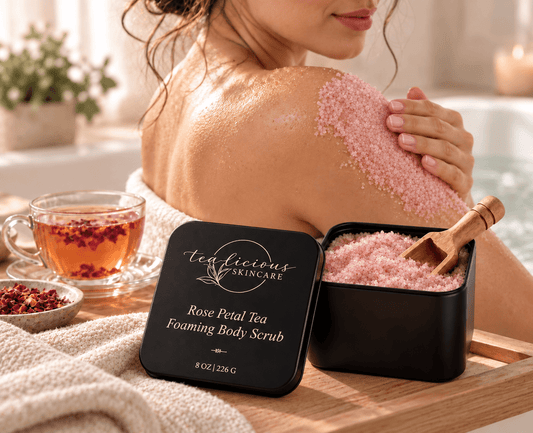 Woman applying Tea-Licious Rose Petal Tea Foaming Body Scrub to her shoulder beside the open scrub tin and a cup of rose tea.
