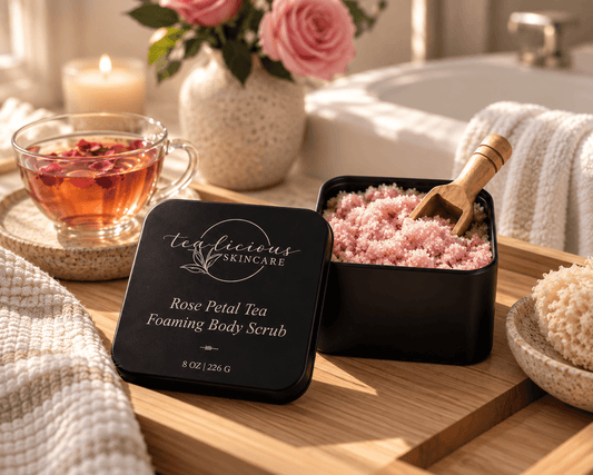Tea-Licious Rose Petal Tea Foaming Body Scrub with pink scrub, wooden scoop, rose tea and spa towels in warm natural light.