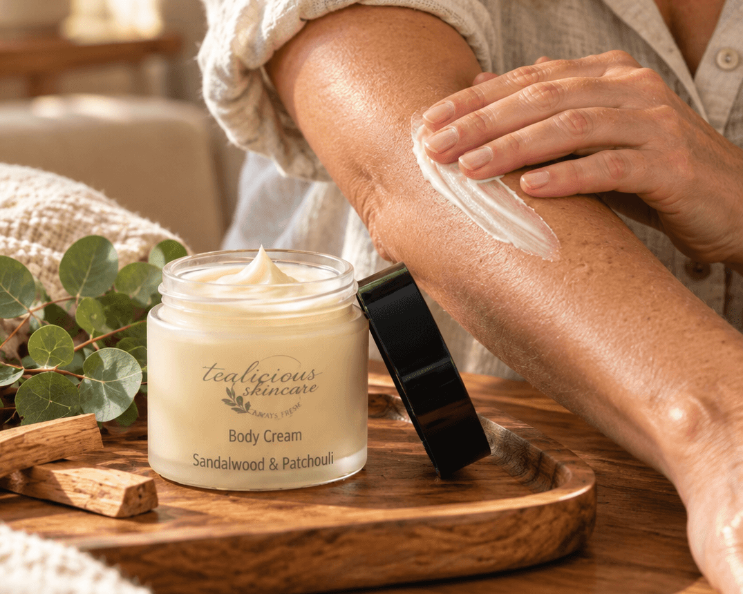 Tea-Licious Sandalwood & Patchouli Body Cream on a wooden tray with eucalyptus and sandalwood in warm natural light.