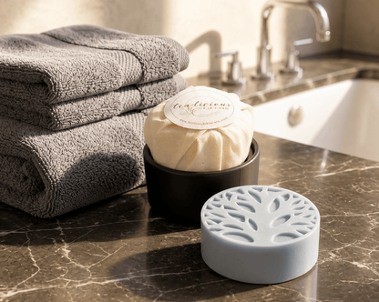 Tea-infused solid lotion bar with a Tree of Life design displayed on a marble bathroom countertop beside folded towels and a travel tin in warm natural light.