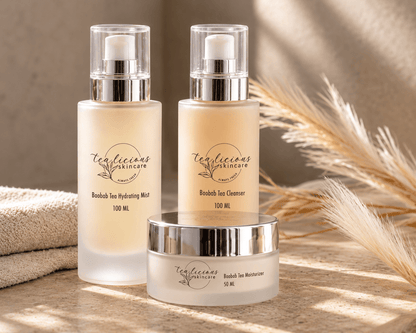 Tea-licious Baobab Tea Cleanser, Hydrating Mist, cleanser and Moisturizer on a stone vanity beside folded towels and dried grasses.