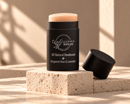 Tea-licious Bergamot Rose & Lavender deodorant in a black oval container with silver lettering, displayed beside its lid on cream stone blocks in warm sunlight.