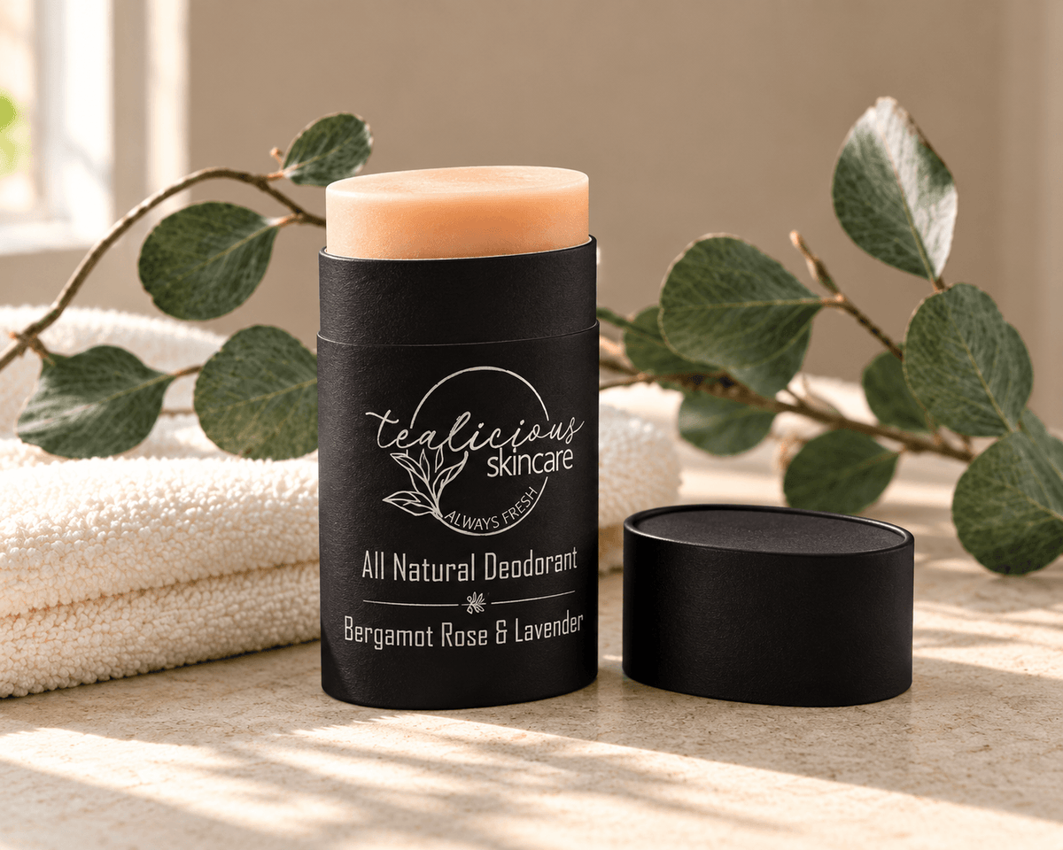 Tea-licious Bergamot Rose & Lavender deodorant in a black oval container with silver lettering, beside its lid, a cream towel and eucalyptus in warm sunlight.