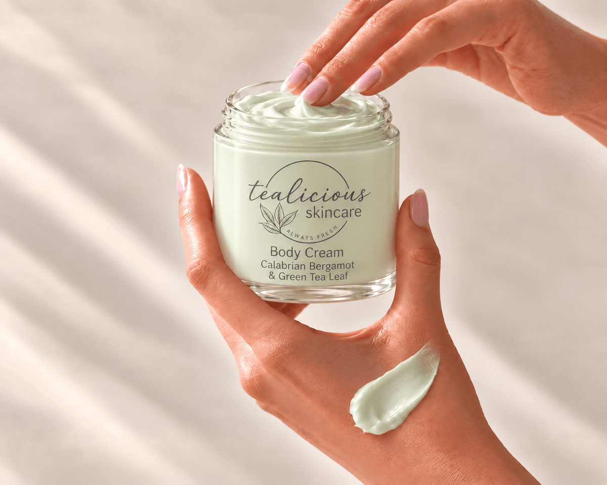 Hands holding an open jar of Calabrian Bergamot & Green Tea Leaf Body Cream, with a fingertip lifting cream and a pale green swatch on the hand.