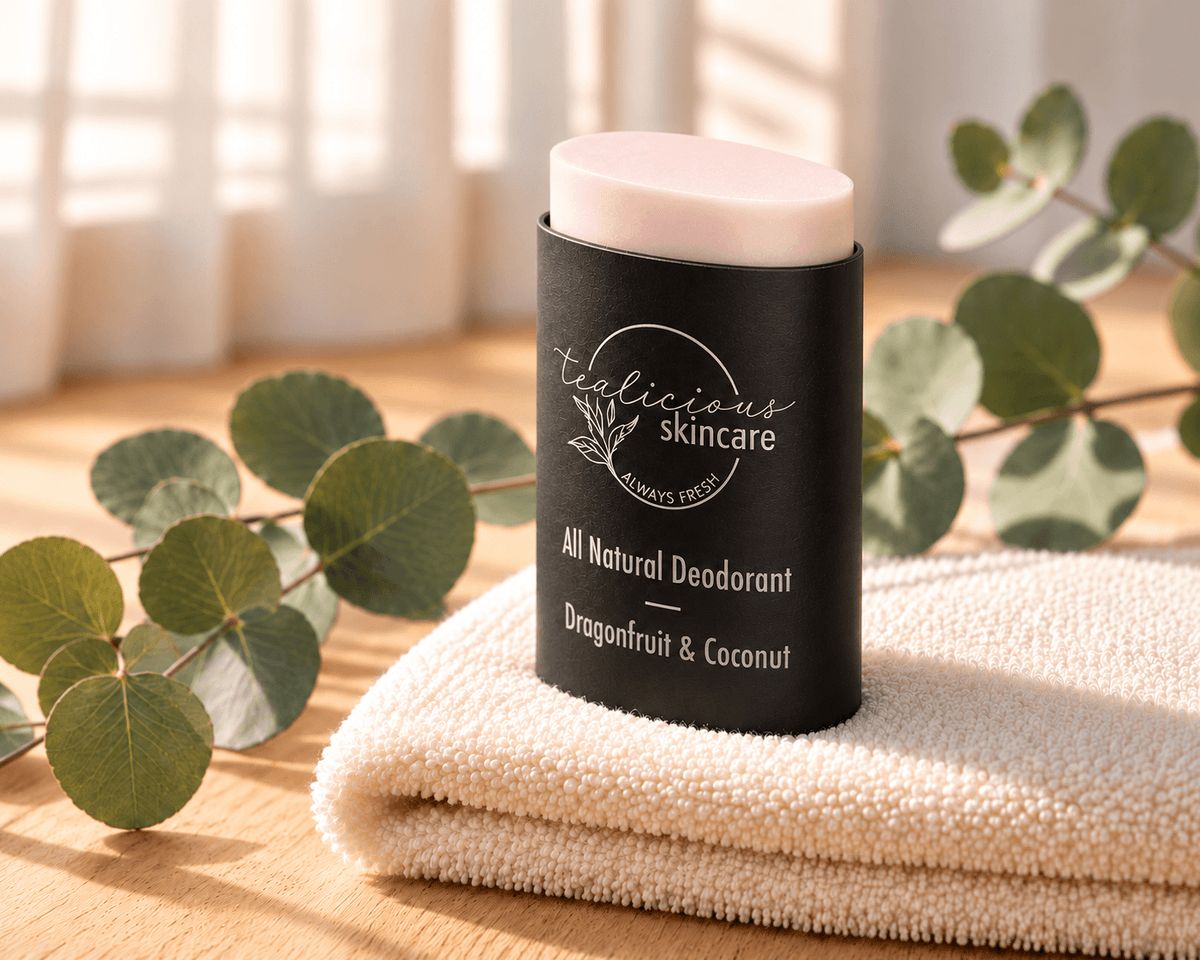 Tea-licious Dragonfruit & Coconut deodorant with a pale blush-pink top in a black oval container, on an ivory towel beside eucalyptus.
