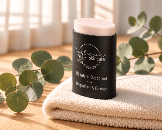 Tea-licious Dragonfruit & Coconut deodorant with a pale blush-pink top in a black oval container, on an ivory towel beside eucalyptus.