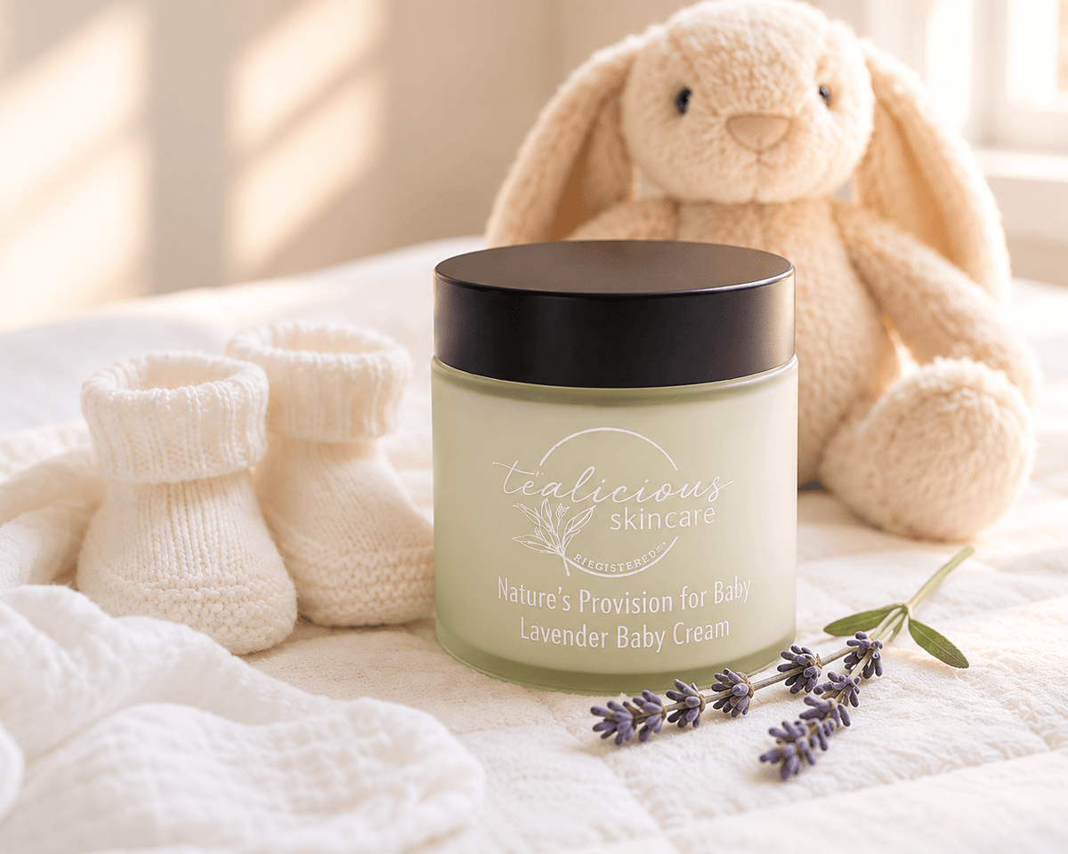 Tea-licious Lavender Baby Cream in a jar beside lavender sprigs, knitted baby booties and a plush bunny.