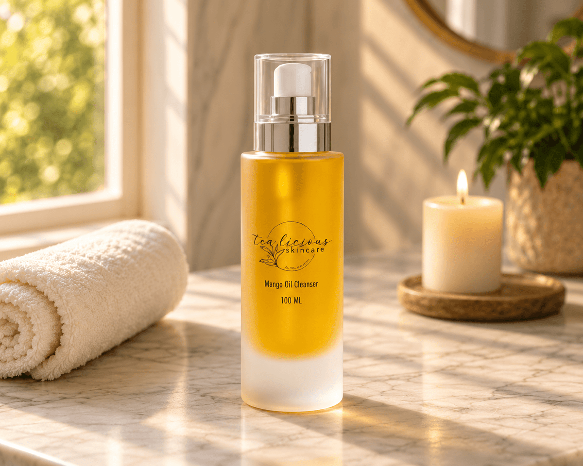 Tea-licious Mango Oil Cleanser in a golden 100 ml pump bottle beside a towel and candle on a sunlit marble vanity.