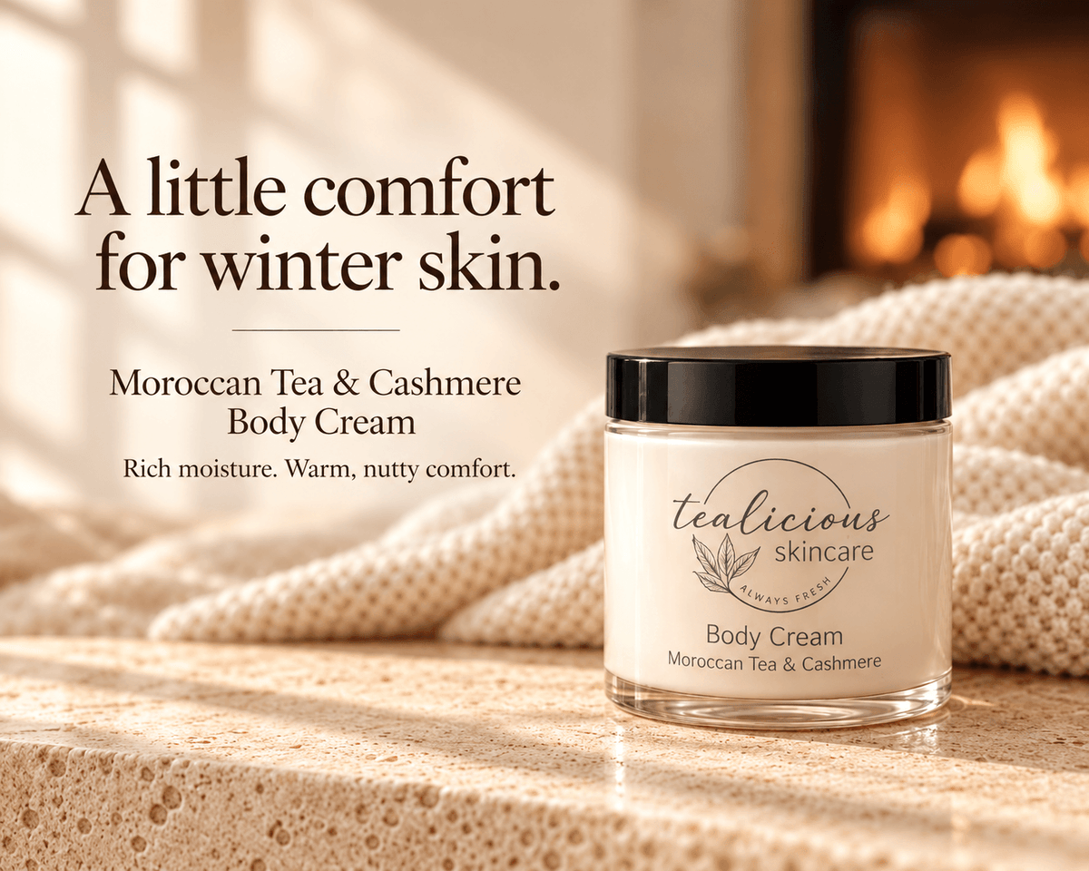 A jar of tealicious skincare Moroccan Tea & Cashmere Body Cream sits on a textured stone surface with a cozy, warm background showing a blurred fireplace and knitted blanket. Text on the left reads 'A little comfort for winter skin.