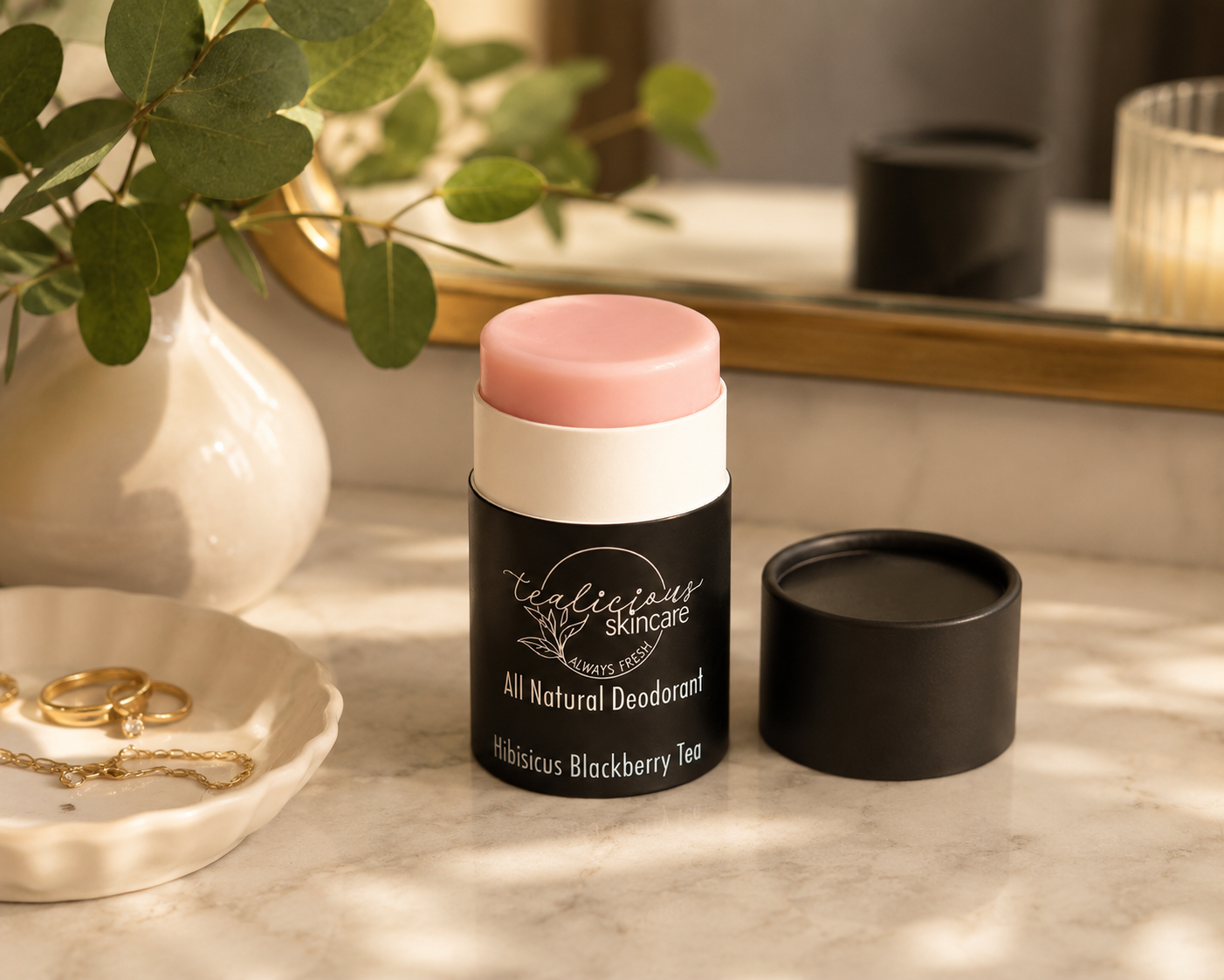 A deodorant stick by Clandestine Skincare in 'Hibiscus Blackberry Tea' scent, shown with its pink cap removed and placed beside the black container on a marble surface.