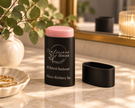 A deodorant stick by Tea-licious Skincare 'Hibiscus Blackberry Tea' scent, shown with its cap removed and placed beside the black container on a marble surface.