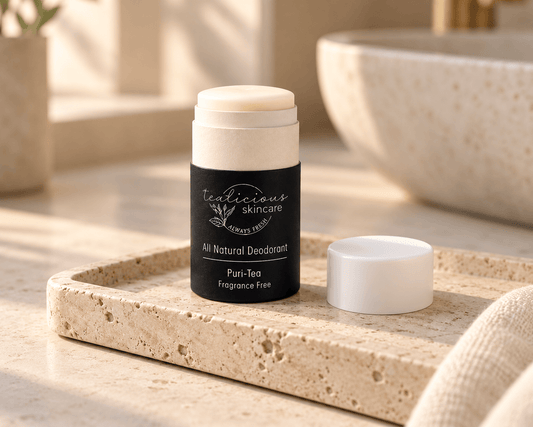 Tea-licious Puri-Tea fragrance-free deodorant with its cap beside it on a travertine tray in soft, warm bathroom light.